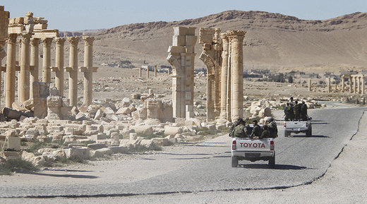Syrian army soldiers drive past the Arch of Triumph in the historic city of Palmyra